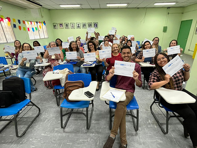 Classroom full of participants, holding up their certificates after completing the course